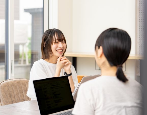 ノートPCを挟んで笑顔で会話する2人の女性。