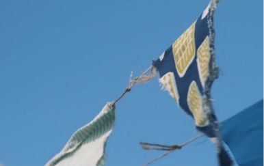 青空にたなびく、紺と黄、白と緑の模様の古びた布の旗。