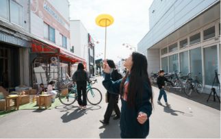 商店まちで黄色い皿回しを見上げる女性