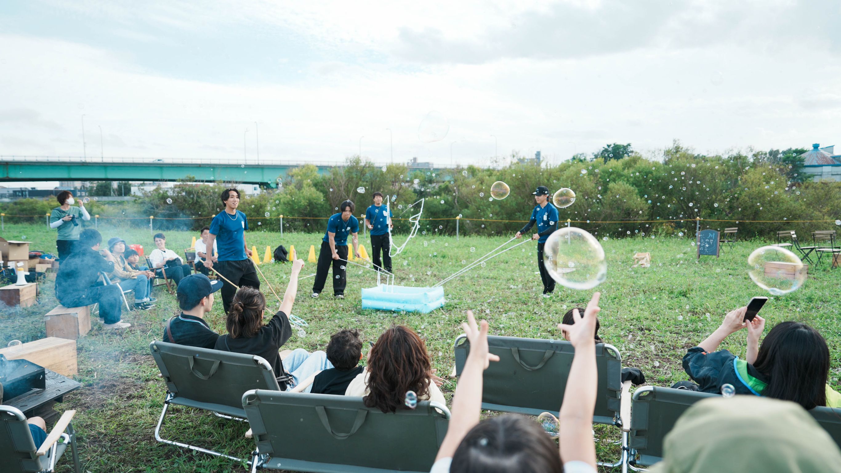 都市の川沿い広場で、大きなシャボン玉を楽しむ人々